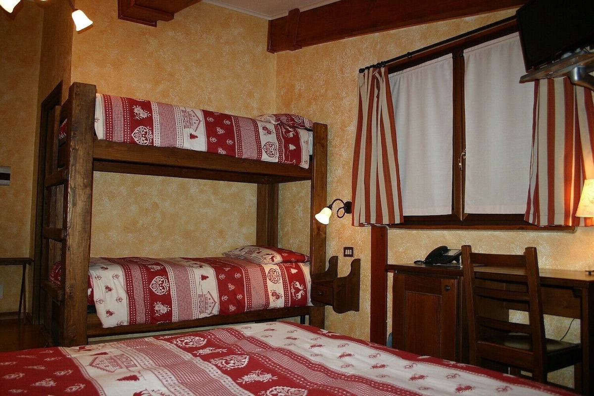 A bunk bed with patterned bedding, a desk with a lamp, and a window with curtains.