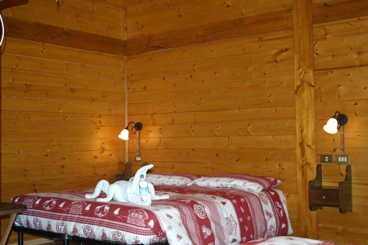 A wooden cabin room with two beds, each with a red and white patterned bedspread, and two wall-mounted lamps.