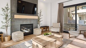 A modern living room with a fireplace, a flat-screen TV mounted on the wall, and a large sliding glass door leading to an outdoor area. - Desert Gem 7 Bedroom Home (St. George)