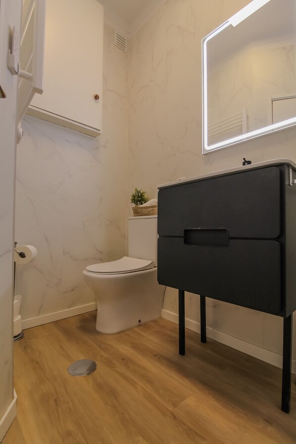 Une salle de bain avec des toilettes blanches, un meuble noir et un miroir avec éclairage intégré.