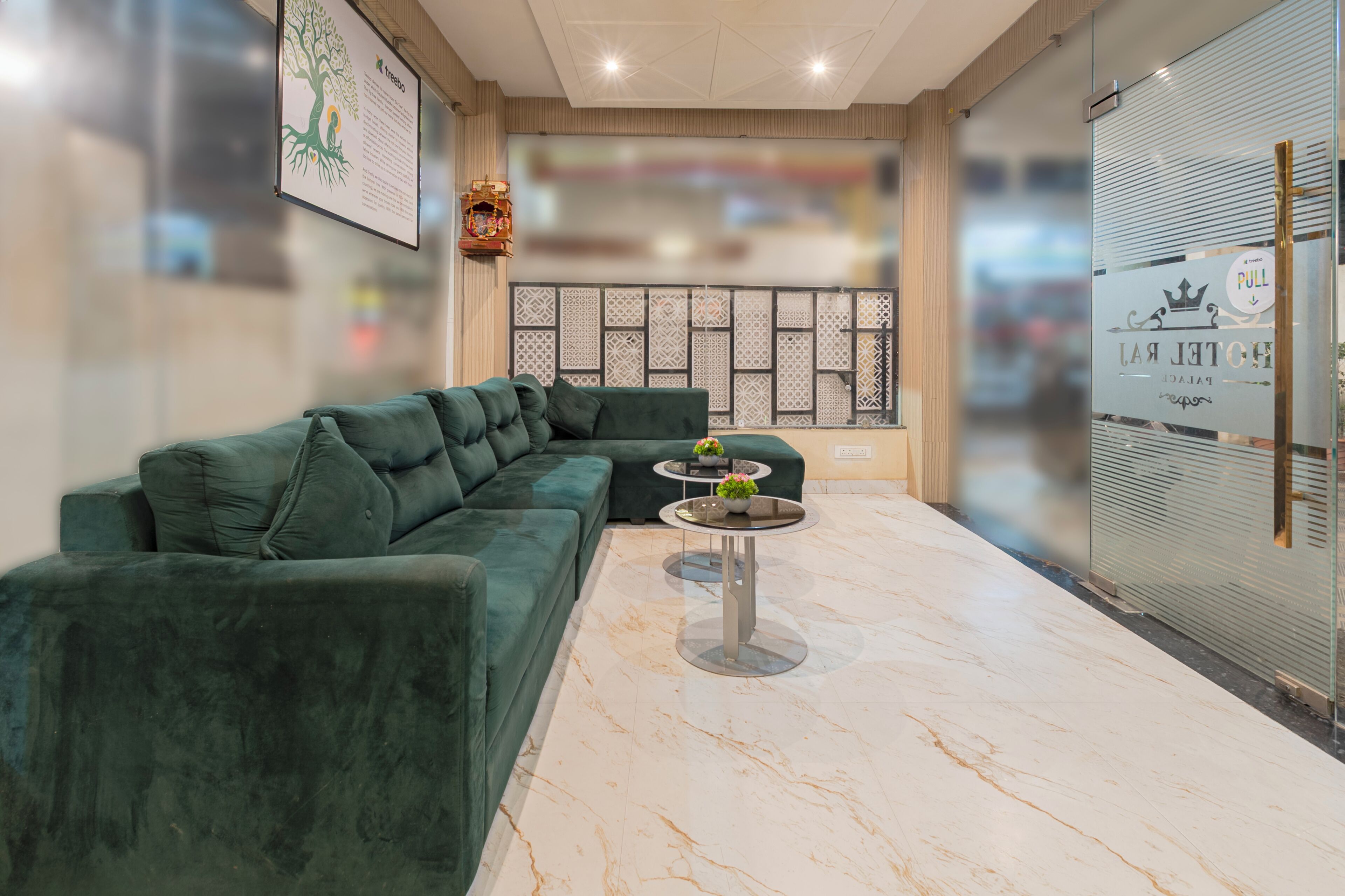 A modern hotel lobby with a green sectional sofa, a small round table with a vase of flowers, and a decorative wall panel.