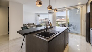 A modern kitchen with a central island, pendant lighting, and a view of the city through large windows. - Carmen - 2 Bedroom Apartment - Downtown (Split)