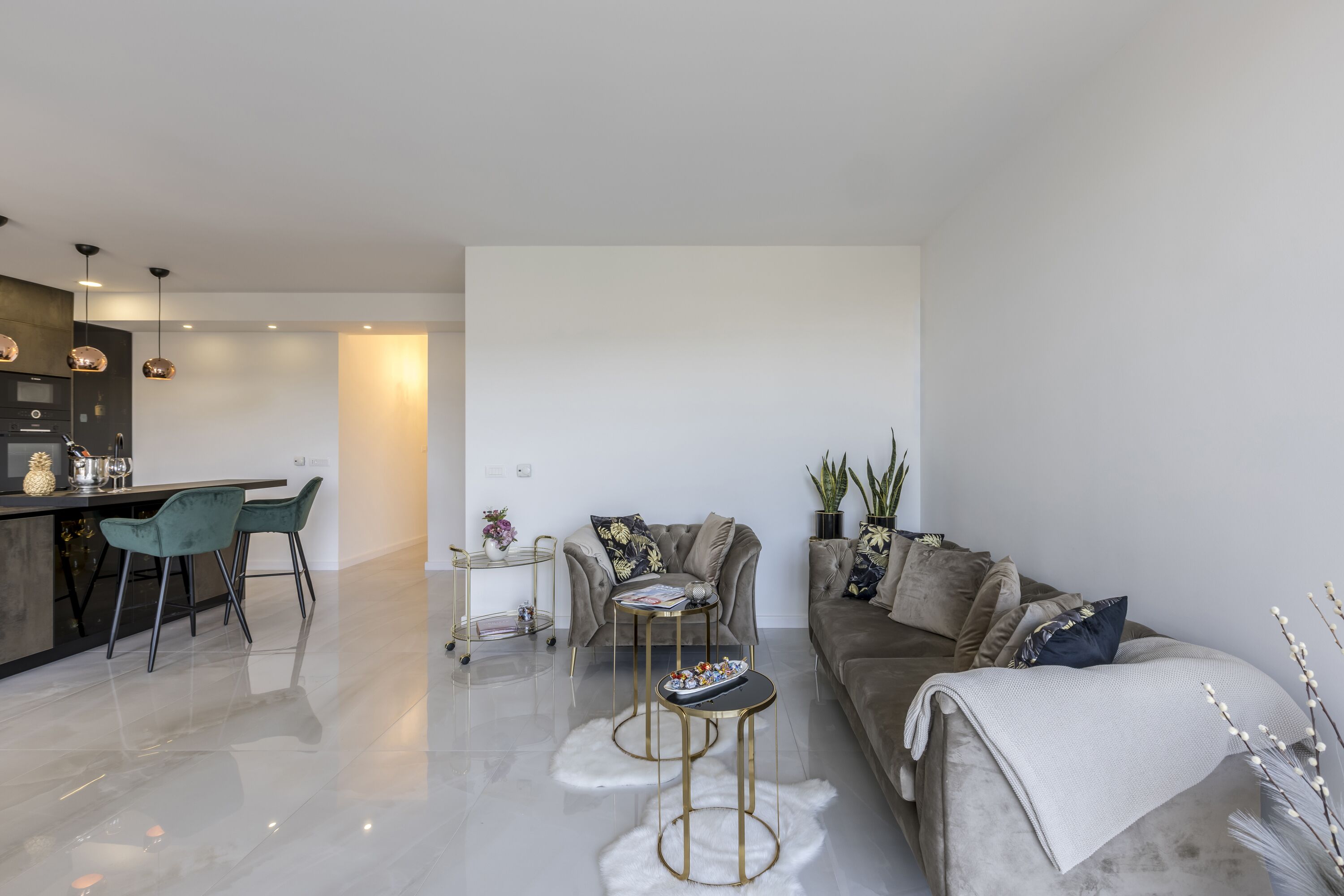 A modern living room with a sofa, coffee table, and chairs. There is a kitchen area with a bar and stools.