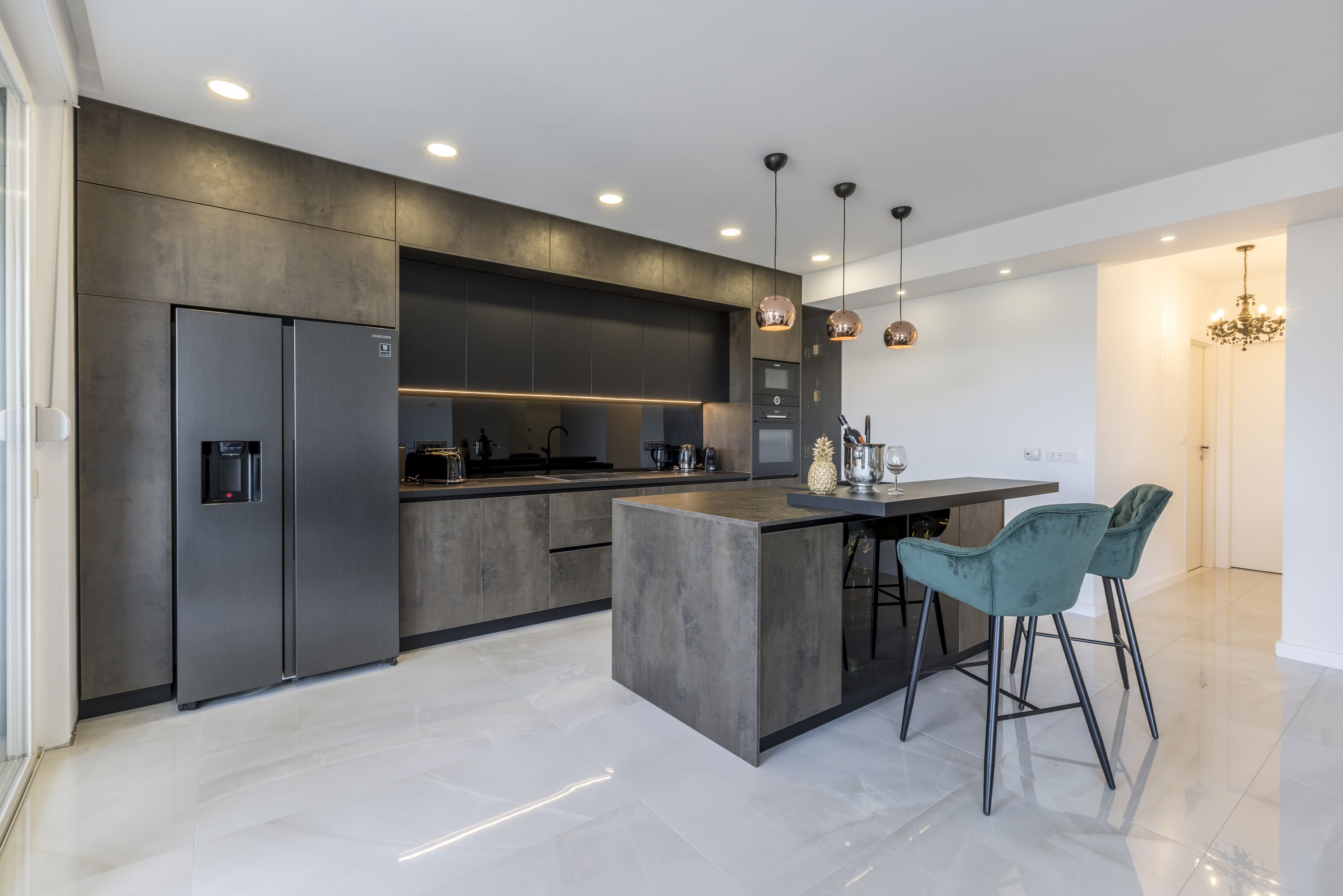 Une cuisine moderne dotée d’un îlot central, d’appareils électroménagers en acier inoxydable et de luminaires suspendus.