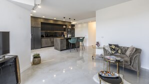 A modern living room with a sofa, a coffee table, and a TV. There is a kitchen area with a dining table and chairs. - Carmen - 2 Bedroom Apartment - Downtown (Split)