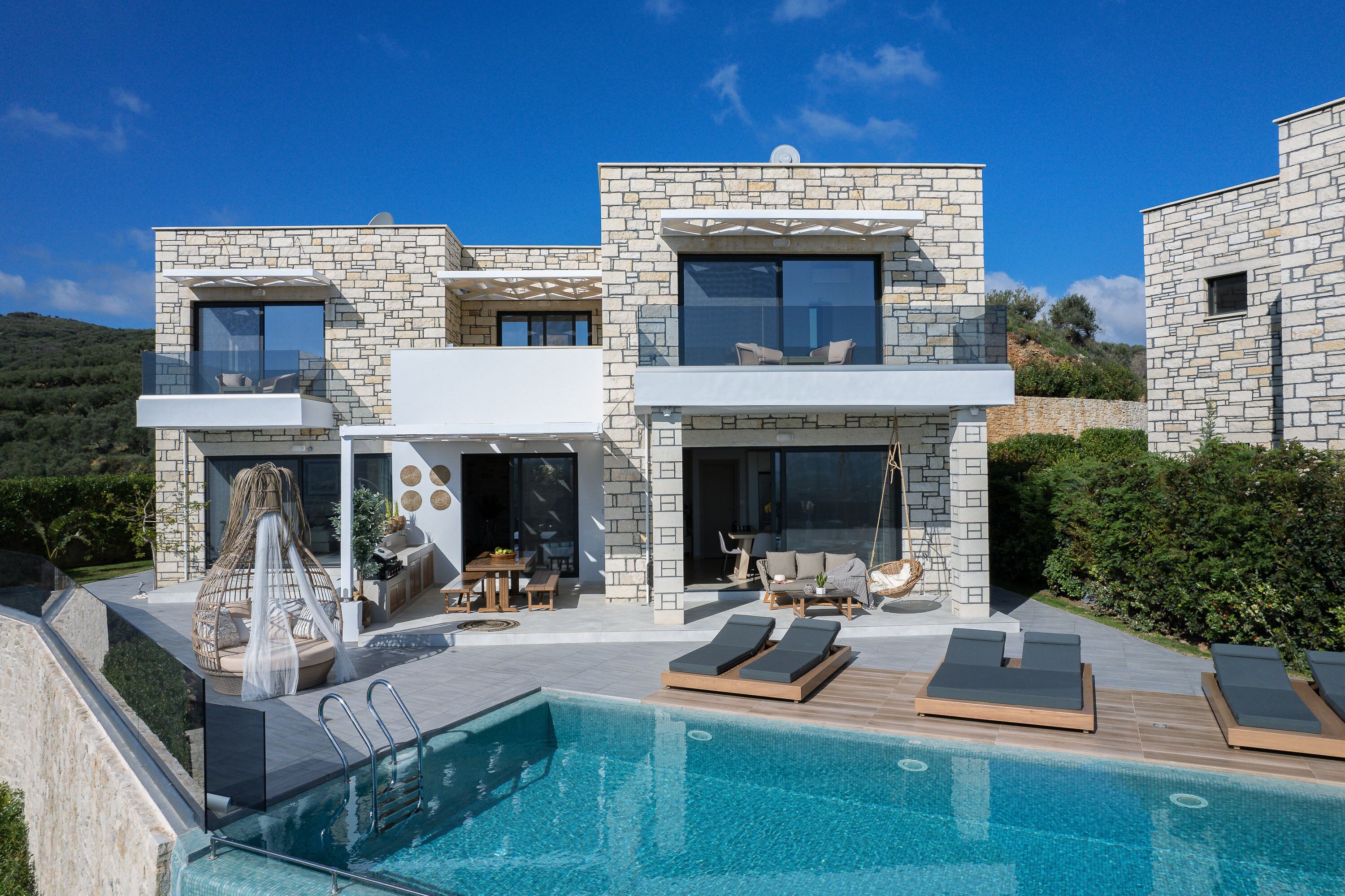 A modern house with a swimming pool, outdoor seating, and a stone facade.