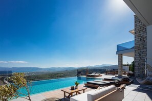 A rooftop infinity pool with a view of the mountains, outdoor seating, and a stone wall. - Argyrie Villas (Kissamos)