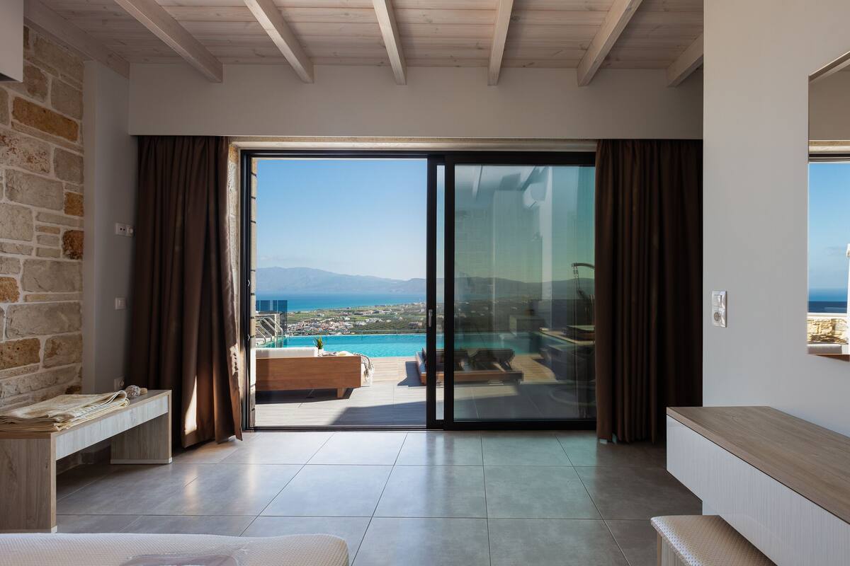 Interior moderno com uma grande porta de vidro deslizante que dá para uma varanda com vista para o mar e montanhas.