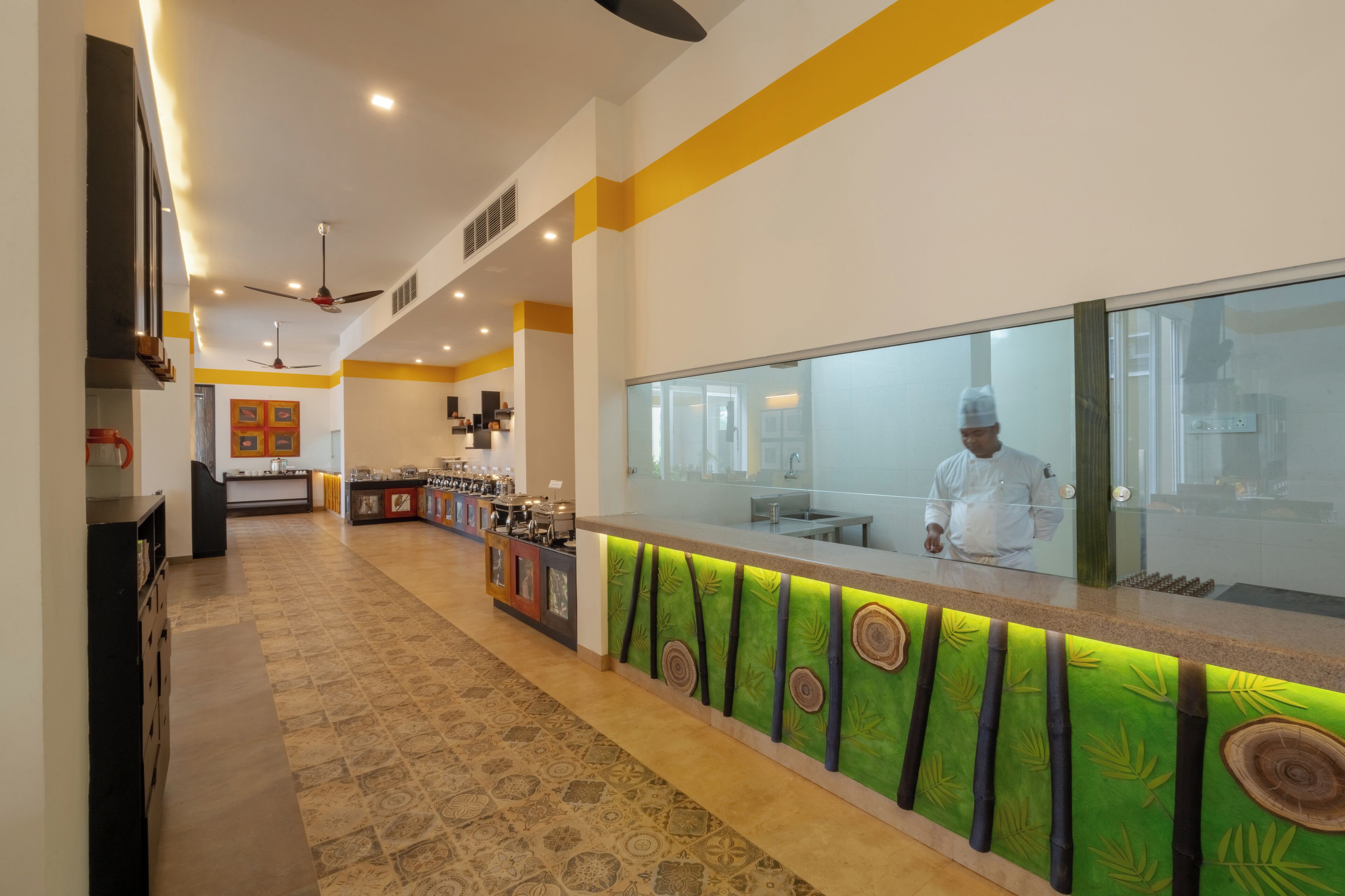 A modern kitchen with a chef at the counter, a patterned floor, and a yellow accent wall.