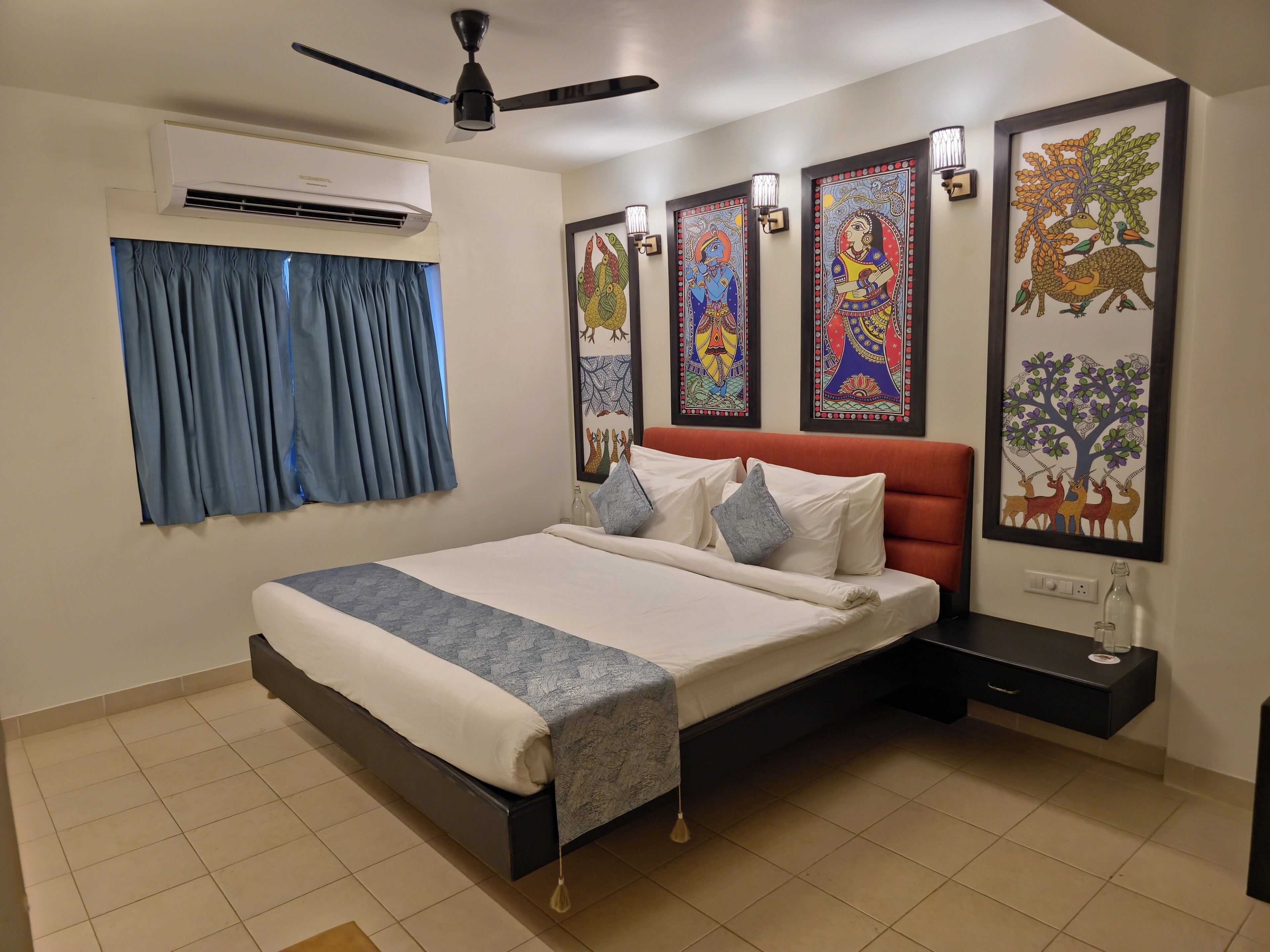 A bedroom with a bed, air conditioning unit, ceiling fan, and artwork on the walls.
