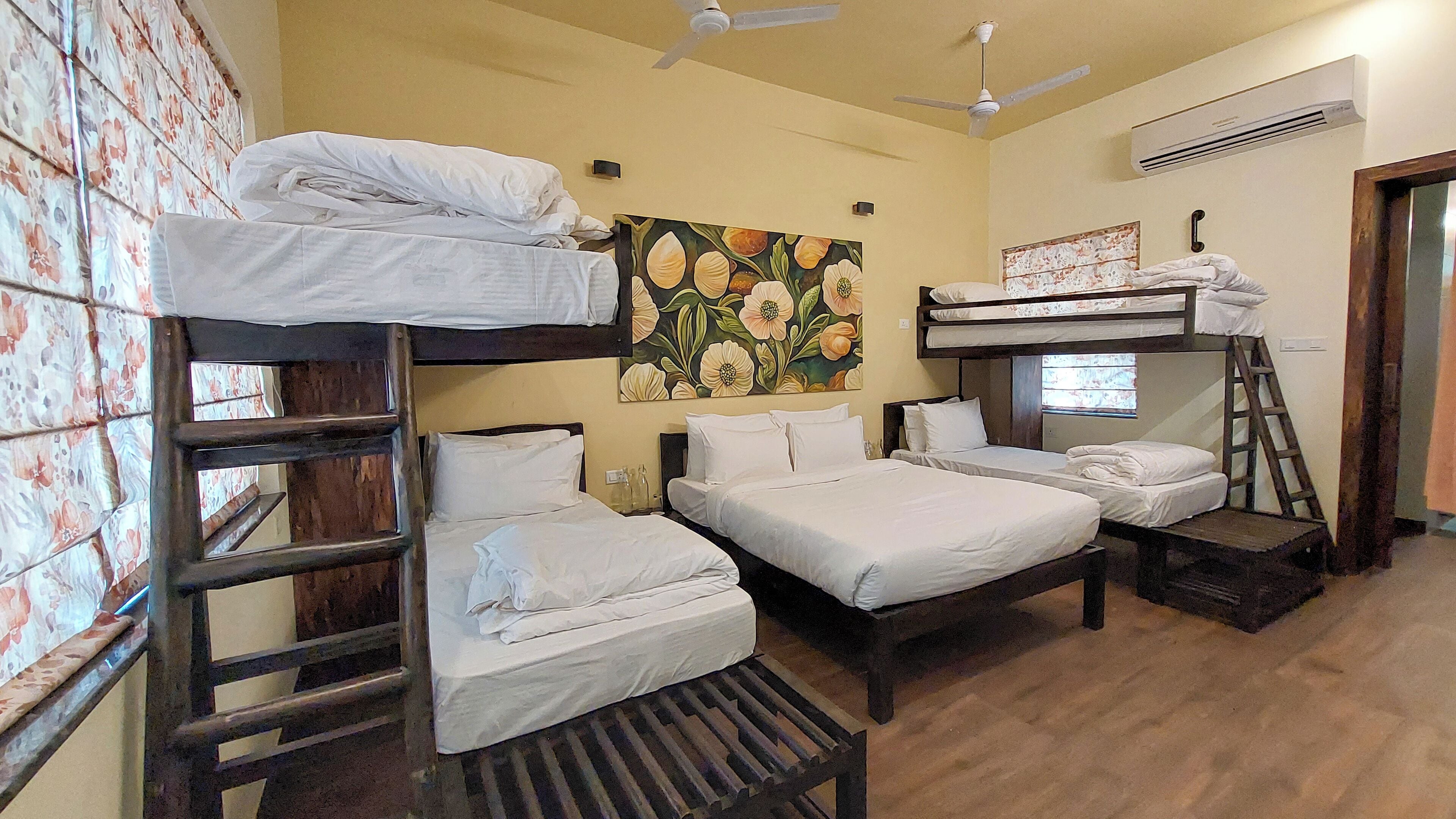 A dormitory room with bunk beds, a ladder, a ceiling fan, an air conditioning unit, and a floral wall decoration.