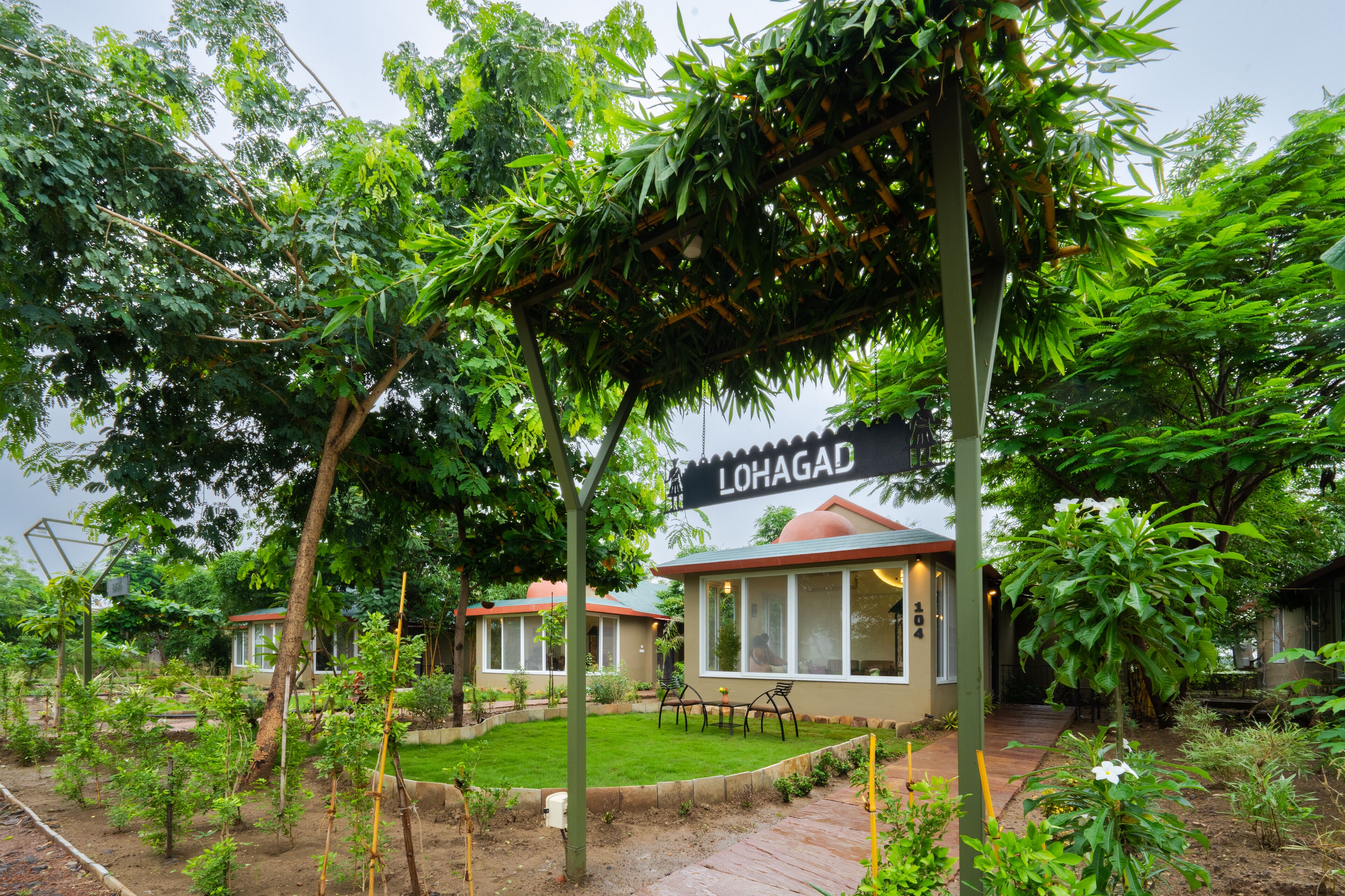 A garden with a pergola, a sign reading "LOHAGAD", and a building with a red roof.