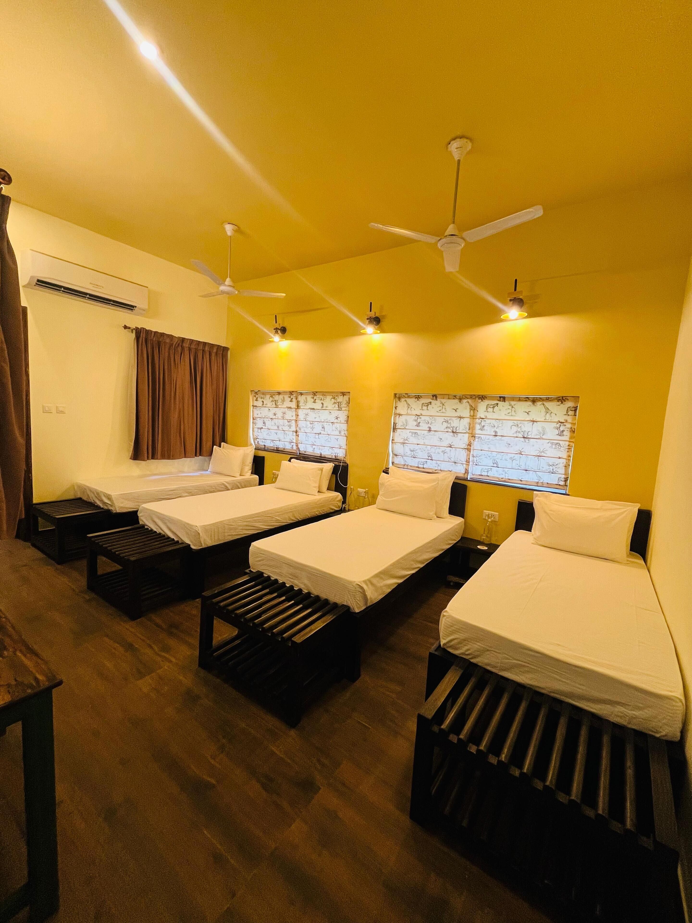 A hotel room with four single beds, a ceiling fan, an air conditioning unit, and a window with patterned curtains.