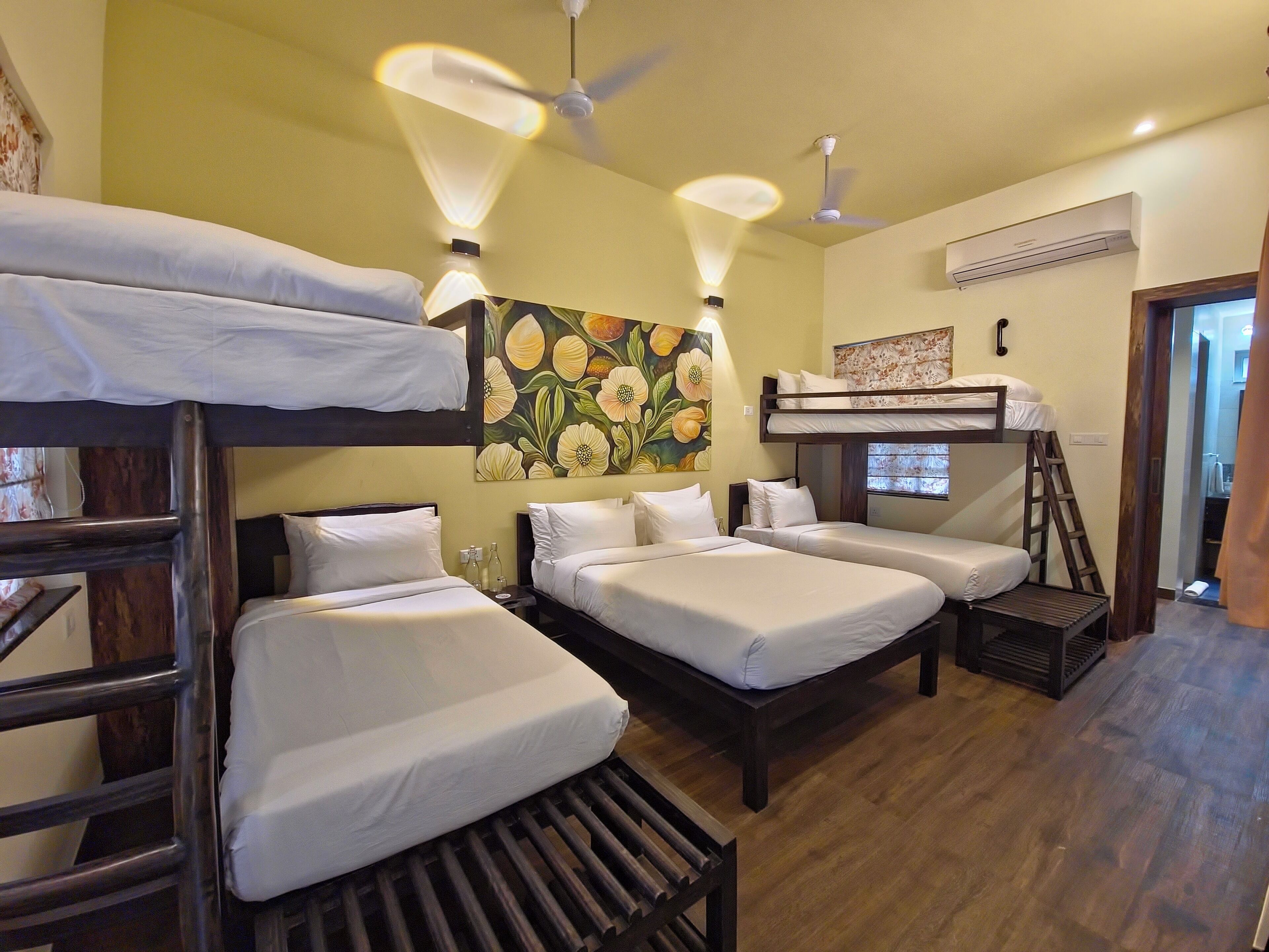Une chambre de type dortoir, avec des lits superposés, une échelle en bois et un ventilateur de plafond.