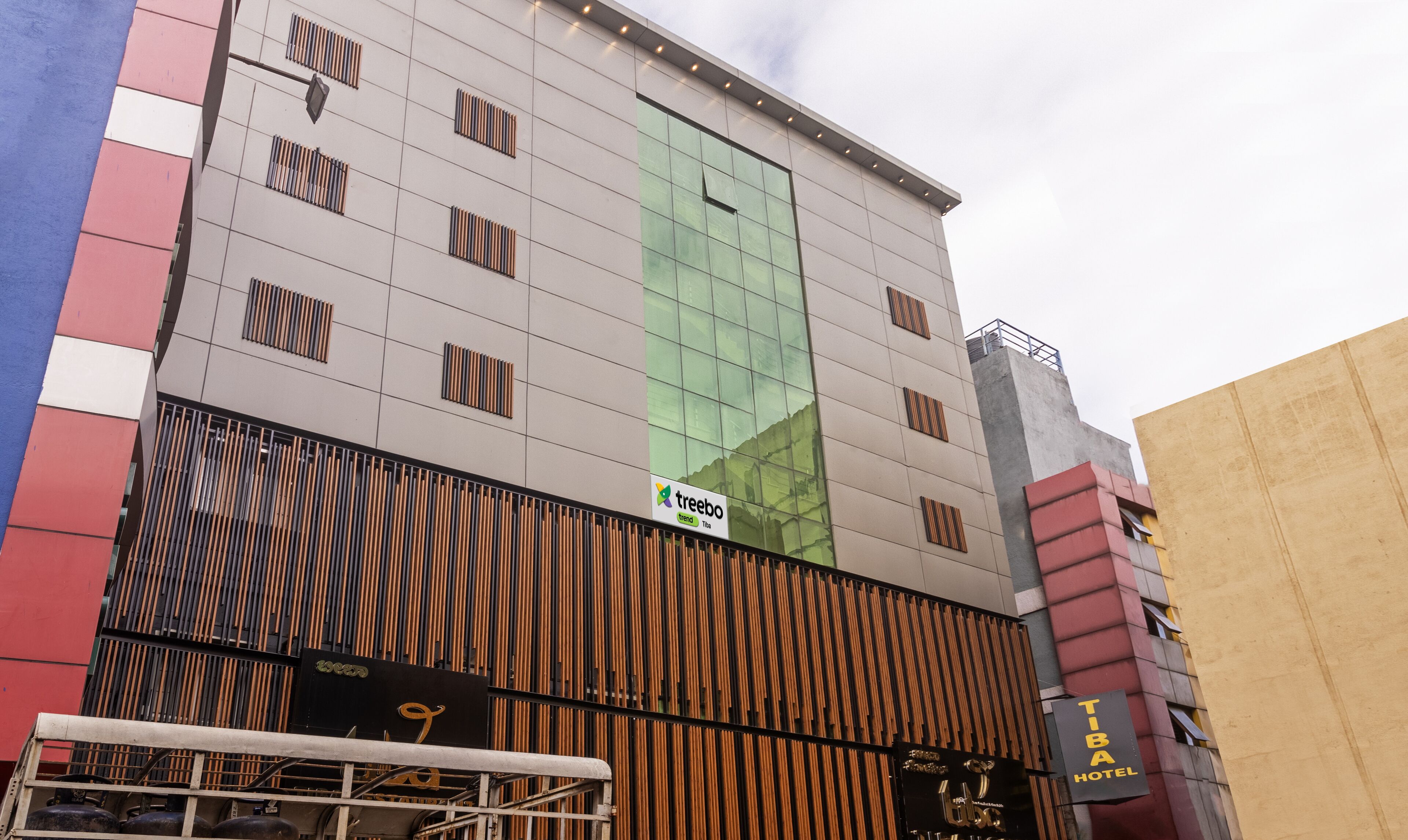 A modern building with a large glass facade, a sign for 'treebo trend Tiba', and a 'TIBA HOTEL' sign.