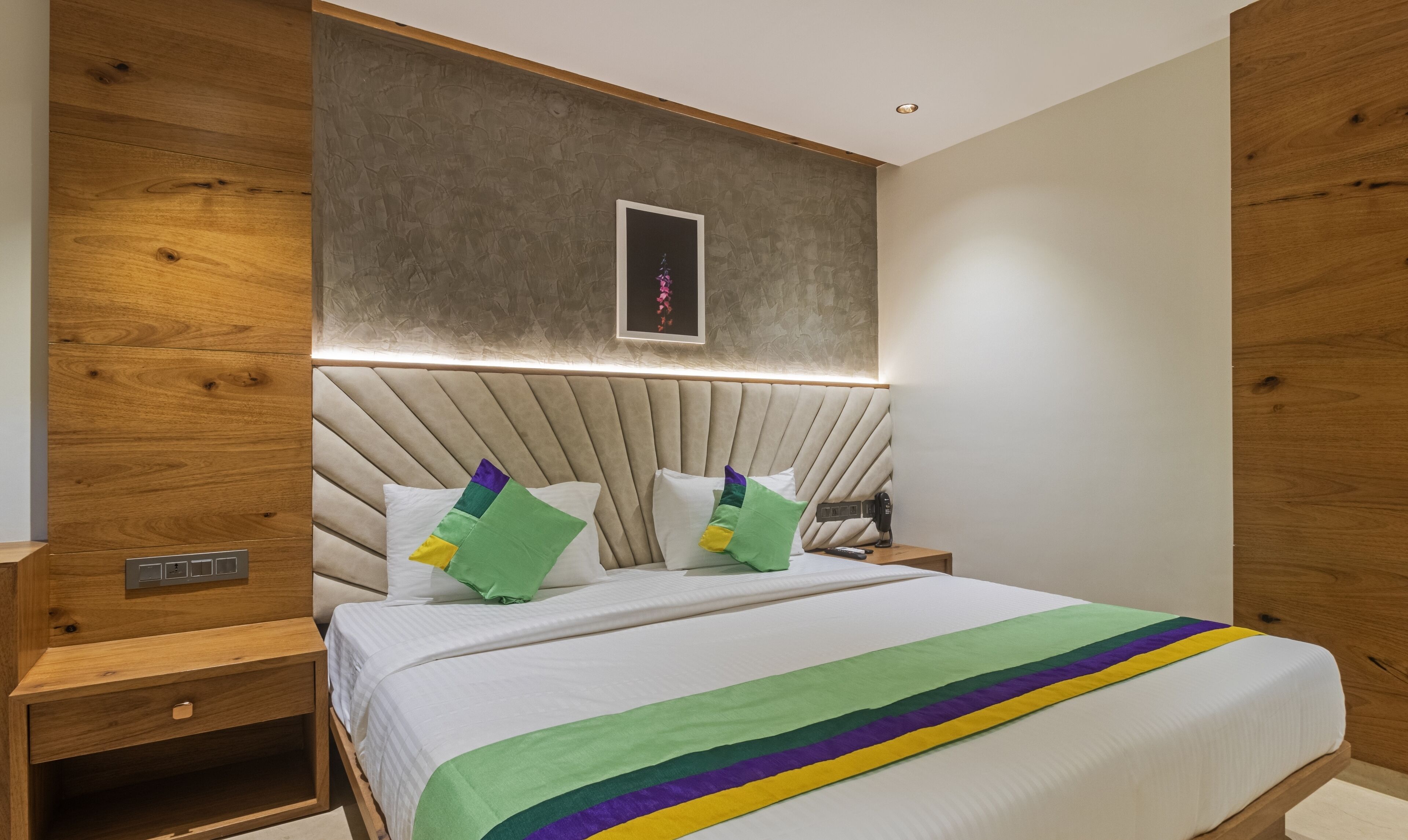A modern bedroom with a wooden headboard, a bed with white bedding, and a colorful blanket.