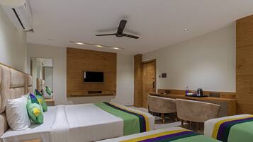 A hotel room with two beds, a desk, chairs, a television, and a ceiling fan.