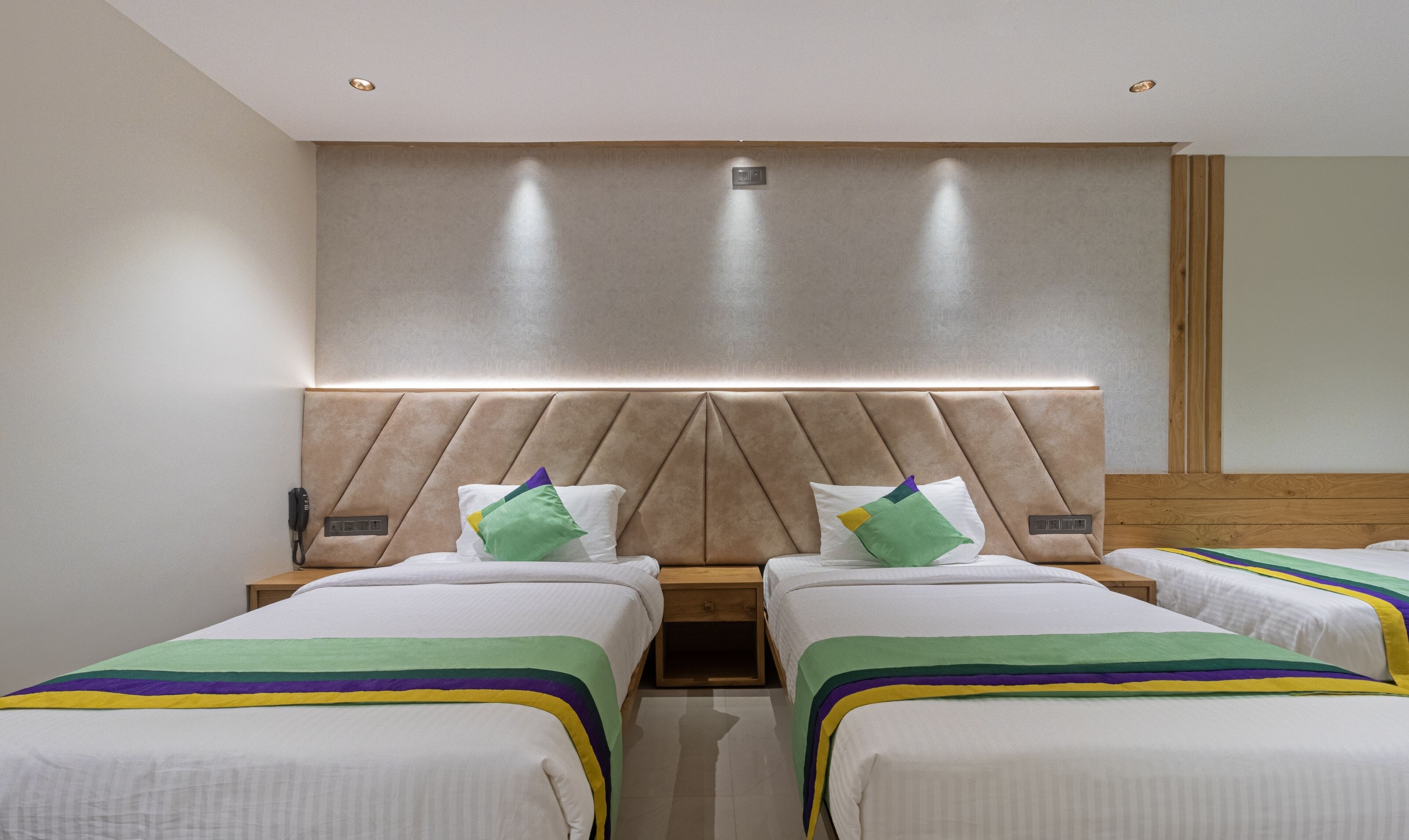 A hotel room with two single beds, a wooden headboard, a bedside table, and a wall-mounted light fixture.