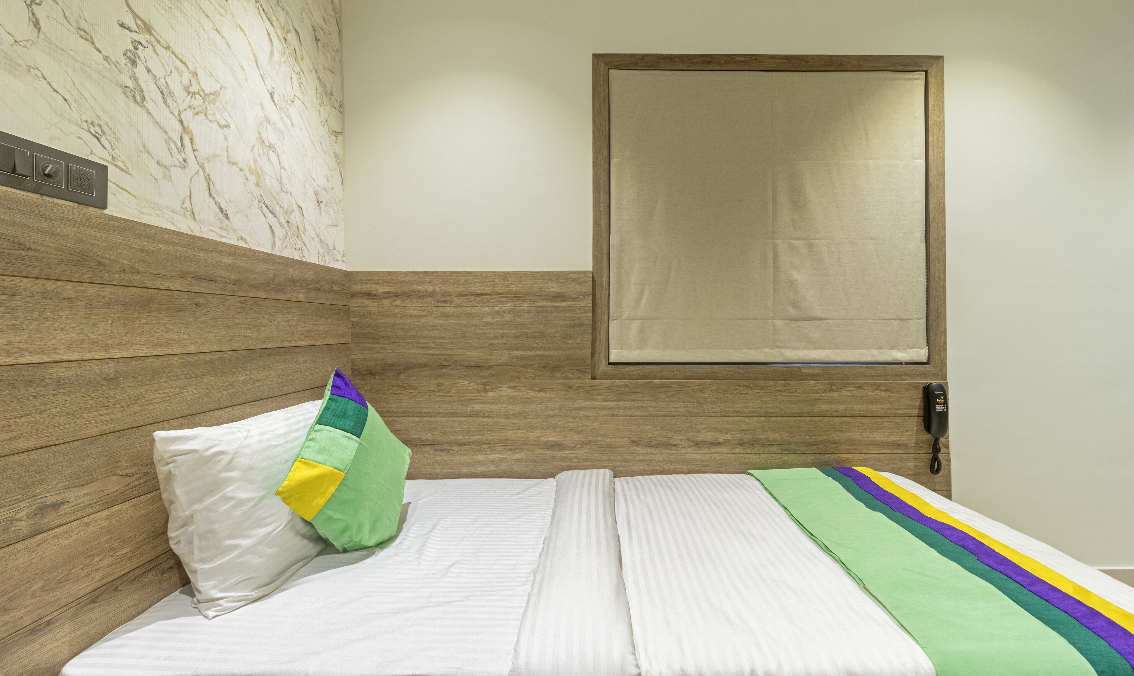 A room with a wooden headboard, a bed with white bedding, a green and yellow pillow, and a wooden door.
