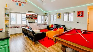 A cozy living room with a pool table, a sofa, and a television mounted on the wall.