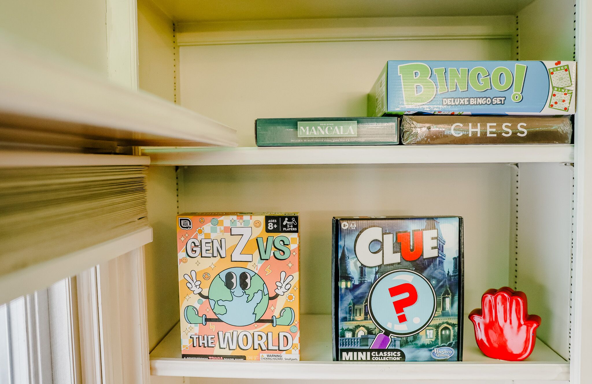En hylde med forskellige brætspil, herunder 'Bingo!', 'Mancala', 'Skak', 'Gen Z vs The World' og 'Clue'.