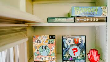 En hylde med forskellige brætspil, herunder 'Bingo!', 'Mancala', 'Skak', 'Gen Z vs The World' og 'Clue'.