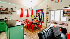 A modern kitchen with a green island, red chairs, and a dining table. There is a painting on the wall and a TV on the right.