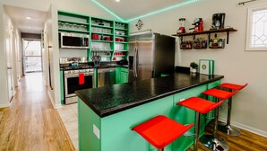 A modern kitchen with green cabinets, a black countertop, and red bar stools.