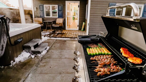 A backyard with a grill, hot tub, and a covered patio area.