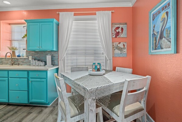 A kitchen with turquoise cabinets, a white dining table, and a window with white curtains. - Beautiful Ocean & Beach Front Condo~Sleeps 5 - Amazing Views! (Galveston)
