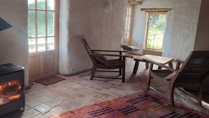 Een knus vertrek met een houtkachel, een houten tafel, een stoel en een raam.