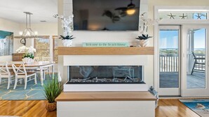 Ein Wohnzimmer mit Fernseher, Kamin, Essbereich und Blick auf den Strand.