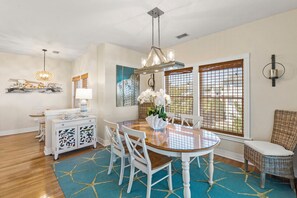 A dining area with a round table, white chairs, a chandelier, and a wicker chair.