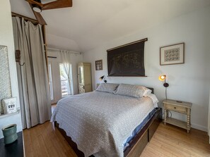 Ein Schlafzimmer mit Bett, Nachttisch, Lampe, einer Weltkarte an der Wand und einem Fenster mit Vorhängen.