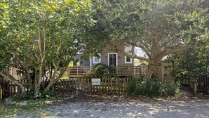A rustic wooden cabin with a gravel driveway and a wooden fence. - Treehouse Charlie: Cute Cottage for Couples or Small Families (Ocracoke)