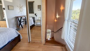 A bedroom with a bed, a desk, and a view of the outdoors through a window. - Treehouse Charlie: Cute Cottage for Couples or Small Families (Ocracoke)