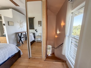 A bedroom with a bed, a desk, and a view of the outdoors through a window. - Treehouse Charlie: Cute Cottage for Couples or Small Families (Ocracoke)