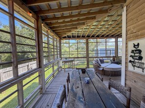 Un espace extérieur abrité, doté de bancs et de tables en bois, de grandes fenêtres et offrant une vue sur la verdure environnante.