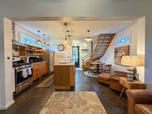 A modern kitchen with a central island, wooden cabinets, and a stainless steel refrigerator. - Treehouse Charlie: Cute Cottage for Couples or Small Families (Ocracoke)