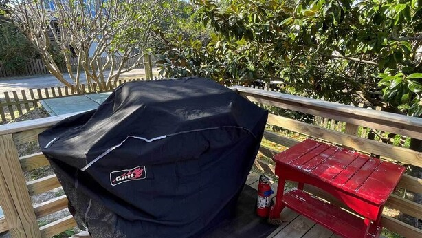A barbecue grill on a wooden deck with a red bench nearby. - Treehouse Charlie: Cute Cottage for Couples or Small Families (Ocracoke)