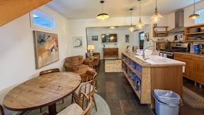 A modern kitchen with a central island, wooden cabinetry, and pendant lighting. - Treehouse Charlie: Cute Cottage for Couples or Small Families (Ocracoke)