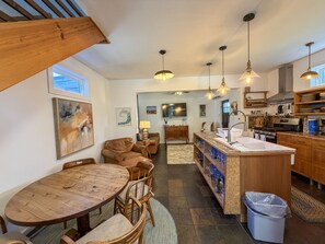 A modern kitchen with a central island, wooden cabinetry, and pendant lighting. - Treehouse Charlie: Cute Cottage for Couples or Small Families (Ocracoke)
