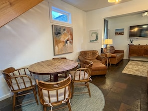 A dining area with a round wooden table and chairs, a brown leather sofa, and a small window above the table.