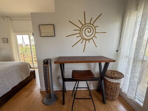 Een kamer met een bed, een elektrische kachel, een tafel met een bankje, een zon decoratie aan de muur en een rieten mand.