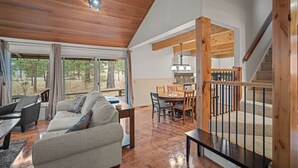 A spacious living area with a wooden ceiling, a dining table, and a staircase leading to an upper level. - Forest Retreat with Access to The Cove (Sunriver)