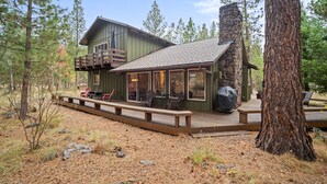 A cabin with a deck, outdoor seating, and a stone chimney. - Forest Retreat with Access to The Cove (Sunriver)