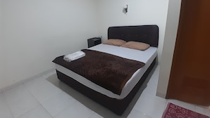 A single bed with a brown headboard and white bedding, a small bedside table, and a wall-mounted light fixture. - AJ Bike Guesthouse Syariah (Yogyakarta)