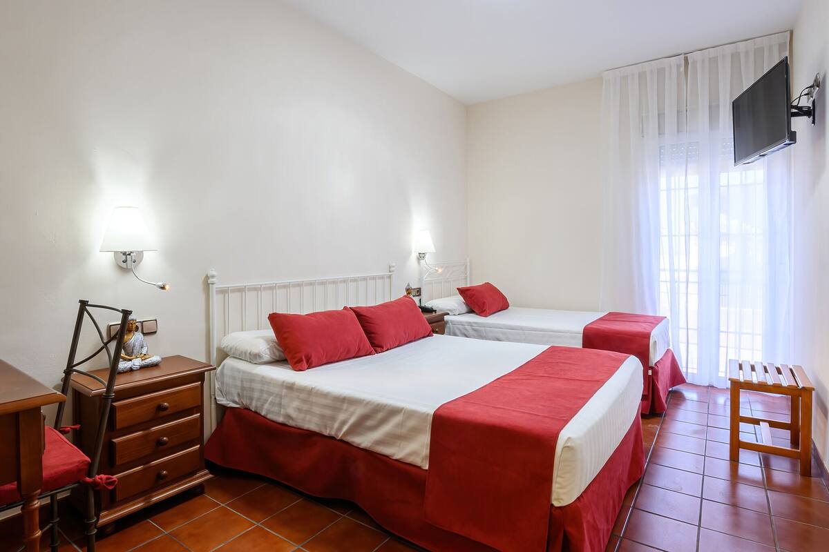 A hotel room with two beds, a wooden dresser, a small table, and a TV mounted on the wall.