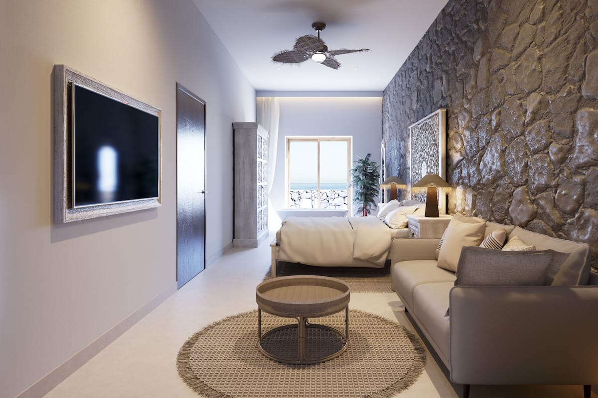 Un salon moderne avec un mur en pierre, un ventilateur de plafond, un grand téléviseur, un canapé, une table basse et une vue sur la mer par une fenêtre.