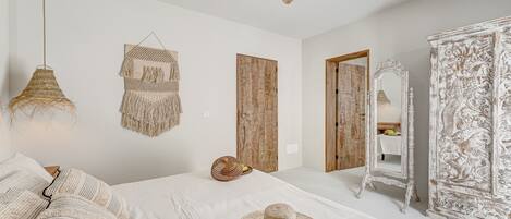 Um quarto com cama, um ventilador de teto, um painel de parede tecido, uma porta de madeira e um guarda-roupa branco.